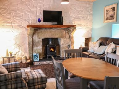 A living room with a stone fireplace and wood-burning stove a wooden dining table with chairs a plaid armchair and a leather sofa with cushions at Mary Larkin's Cottage Rostrevor near Newry