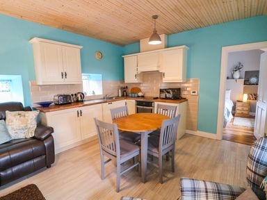 A kitchen with white cabinets a round wooden table with four chairs a brown leather sofa and a plaid armchair at Mary Larkin's Cottage Rostrevor near Newry