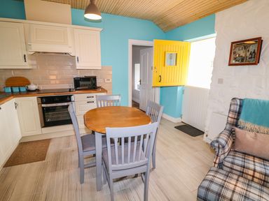 A kitchen with a wooden table and four chairs next to a yellow door and a plaid armchair at Mary Larkin's Cottage in Rostrevor near Newry