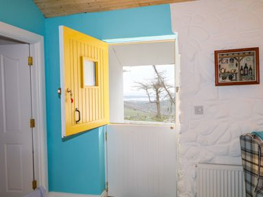 An interior view of a room with a half yellow and half white door opening to a landscape outside at Mary Larkins Cottage Rostrevor near Newry