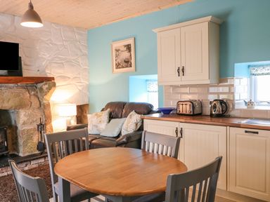 A kitchen dining area with wooden table and chairs near a stone fireplace and leather sofa at Mary Larkin's Cottage Rostrevor near Newry