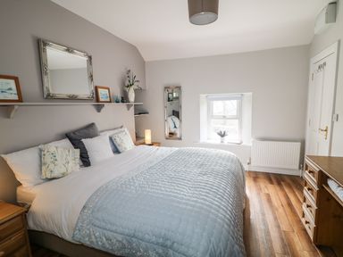 A bedroom with a large bed a wooden chest of drawers and a window at Mary Larkins Cottage in Rostrevor near Newry