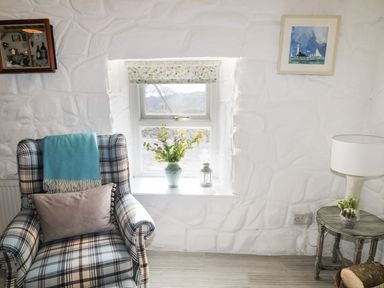 A sitting area with a plaid armchair next to a window with flowers on the sill and a small table with a lamp and plant at Mary Larkins Cottage in Rostrevor near Newry