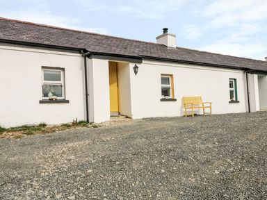A white cottage with a yellow door and bench a gravel area in front at Mary Larkin's Cottage in Rostrevor near Newry