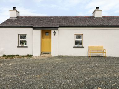 A white cottage with a yellow door two windows and a yellow bench outside at Pat White's Cottage in Rostrevor