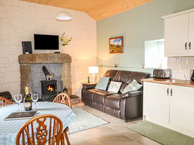 A living room with a round table set for drinks a leather sofa a wood stove and kitchen cabinets at Pat Whites Cottage in Rostrevor