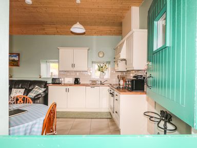 A kitchen with white cabinets a wooden ceiling and tiled floor seen through a green half door at Pat Whites Cottage in Rostrevor