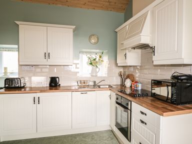 A kitchen with white cabinets wooden countertops and appliances at Pat Whites Cottage in Rostrevor