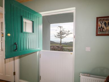 A half-open green and white stable door with a view of a tree and picnic table outside at Pat White's Cottage Rostrevor
