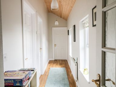 A hallway with white doors wooden floor a light blue rug two windows with a radiator below at Pat White's Cottage in Rostrevor