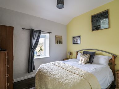 A bedroom with a double bed with pillows and a quilt next to a window with curtains at Pat White's Cottage Rostrevor