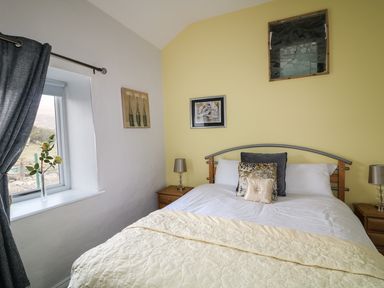 A bedroom with a bed pillows bedside tables lamps and a window with curtains at Pat White's Cottage in Rostrevor
