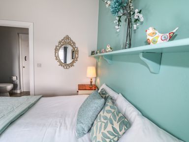 A bedroom with a bed pillows a bedside table lamp a wall mirror and a shelf with decorative birds and flowers at Pat Whites Cottage Rostrevor