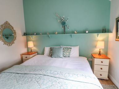 A bedroom with a double bed between two bedside tables with lamps and a shelf with decorations above the bed at Pat White's Cottage in Rostrevor
