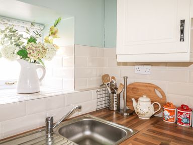 A kitchen sink with a faucet beside a window with flowers in a white jug on the sill at Pat White's Cottage Rostrevor