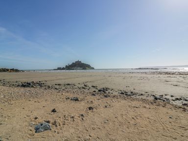 A sandy beach with scattered rocks and an island with buildings in the background at Beachcomber in Marazion