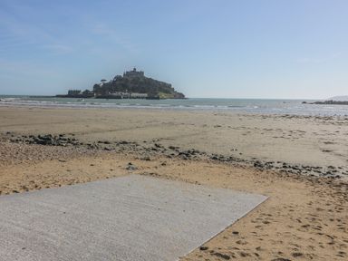 A sandy beach with rocks and a castle on an island in the sea at Beachcomber in Marazion