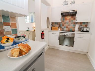 A kitchen with white cabinets a plate of croissants a toaster and a tray with snacks at Beachcomber in Marazion