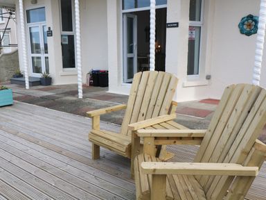 Two wooden chairs on a deck outside a building with white walls and glass doors at Beachcomber in Marazion