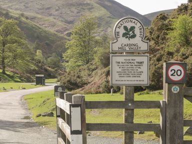 An entrance gate with National Trust signs and a speed limit sign by a gravel road in a valley with hills and trees at Shepherd's Rest in Montgomery