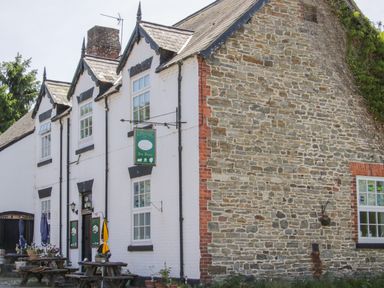 A stone and brick building with white painted walls and outdoor wooden tables and umbrellas at Shepherd's Rest in Montgomery