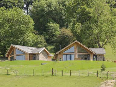 Two wooden and stone houses on a grassy hill with trees in the background at Shepherd's Rest in Montgomery