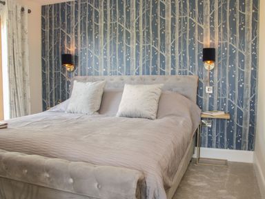A bedroom with a grey bed and pillows against a wallpapered wall with tree designs at Shepherd's Rest in Montgomery