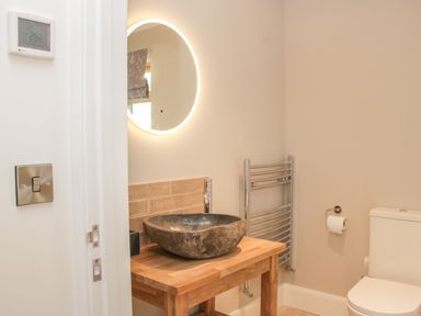 A bathroom with a round illuminated mirror a stone sink on a wooden countertop a chrome towel rack and a toilet at Shepherd's Rest in Montgomery