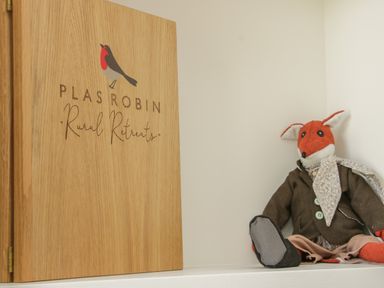 A wooden box with a robin logo and text Plas Robin Rural Retreats next to a stuffed fox toy wearing a brown jacket and a scarf at Shepherd's Rest in Montgomery