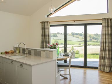 A kitchen area with a sink and counter next to a dining table by large glass doors showing a countryside view at Shepherd's Rest in Montgomery