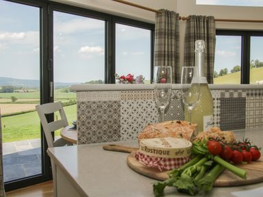 A kitchen countertop with bread cheese vegetables and champagne glasses overlooking countryside through large windows at Shepherd's Rest in Montgomery