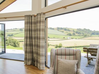 A room with plaid curtains and an armchair next to large glass doors opening to a countryside view at Shepherd's Rest in Montgomery