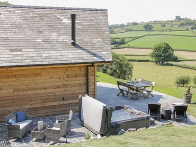 An outdoor patio with a hot tub seating area and dining table overlooking green fields at Shepherd's Rest in Montgomery