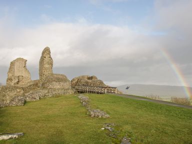 Ruins of an old stone structure with a wooden bridge and a rainbow in the sky