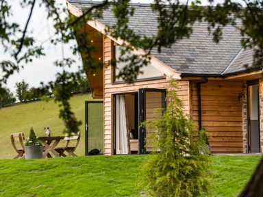 An exterior view of a wooden house with open glass doors and outdoor wooden table and chairs on green grass at Shepherd's Rest in Montgomery