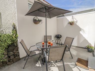 An outdoor patio with a round glass table and four chairs under a large umbrella at Emblestones in Embleton
