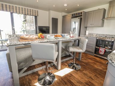 A kitchen with grey cabinets a granite countertop and two grey bar stools at Emblestones in Embleton