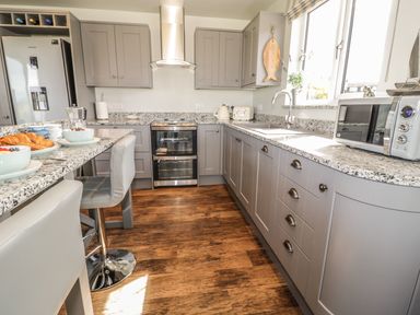 A kitchen with gray cabinets a stainless steel refrigerator an oven a microwave and a breakfast bar with stools at Emblestones in Embleton