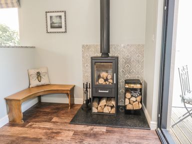 A wood burning stove with logs stored underneath and on the side next to a wooden corner bench with a bee cushion at Emblestones in Embleton