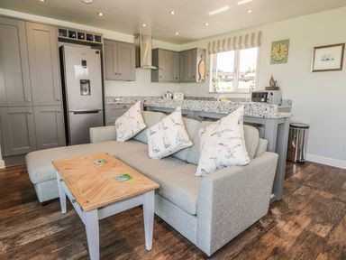 A kitchen with grey cabinets and a silver refrigerator next to a grey sofa with printed cushions and a wooden coffee table at Emblestones in Embleton