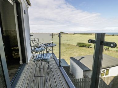 A balcony with a metal table and two chairs overlooking fields and a distant sea at Emblestones in Embleton