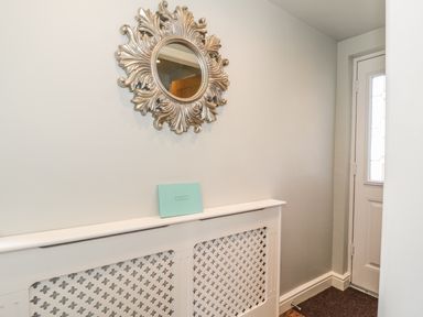 A hallway with a decorative mirror above a radiator cover and a white door at Emblestones in Embleton
