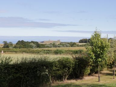 A rural landscape with trees hedges and grassy fields with distant ruins at Emblestones in Embleton