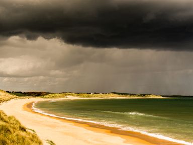 A beach with yellow sand and green water under dark clouds at Emblestones in Embleton