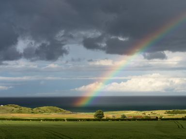 A green field with trees and hills by the sea under a cloudy sky with a rainbow at Emblestones in Embleton
