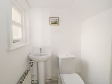 A bathroom with a pedestal sink, toilet, radiator, window, and a small framed picture on the wall at 20 Ulwell Road Swanage