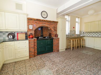 A kitchen with cream cabinets green stove in a brick alcove and wooden stools at a counter at 20 Ulwell Road Swanage