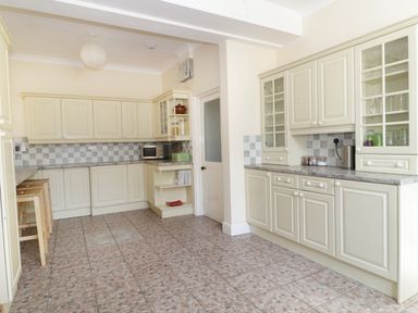 A kitchen with cream cabinets tiled floor and three wooden stools at 20 Ulwell Road Swanage