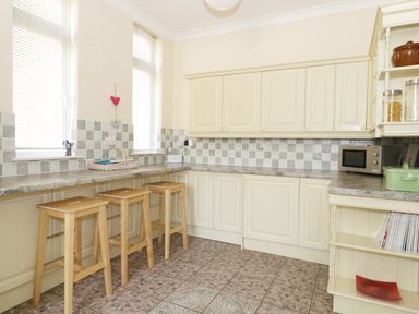 A kitchen with cream cabinets three wooden stools tiled floor and a microwave at 20 Ulwell Road in Swanage