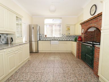A kitchen with cream cabinets a stainless steel refrigerator a window above a sink and a green stove set in a brick alcove at 20 Ulwell Road in Swanage